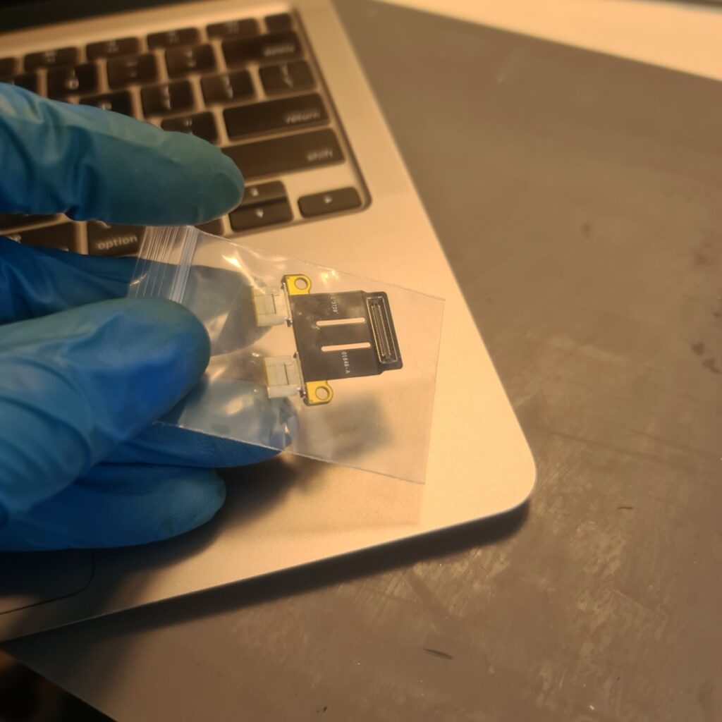 A 2020 MacBook Air M1 connected via USB-C cable to a host Mac undergoing a Apple Configurator DFU restore procedure to fix file system corruption.