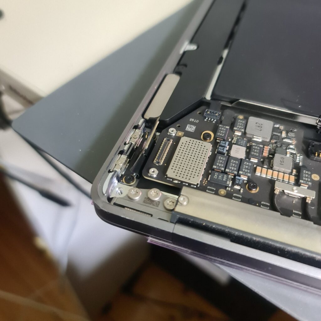 Interior view of a 2020 MacBook Air M1 during diagnostics, showing the modular USB-C port flex cable disconnected from the logic board.